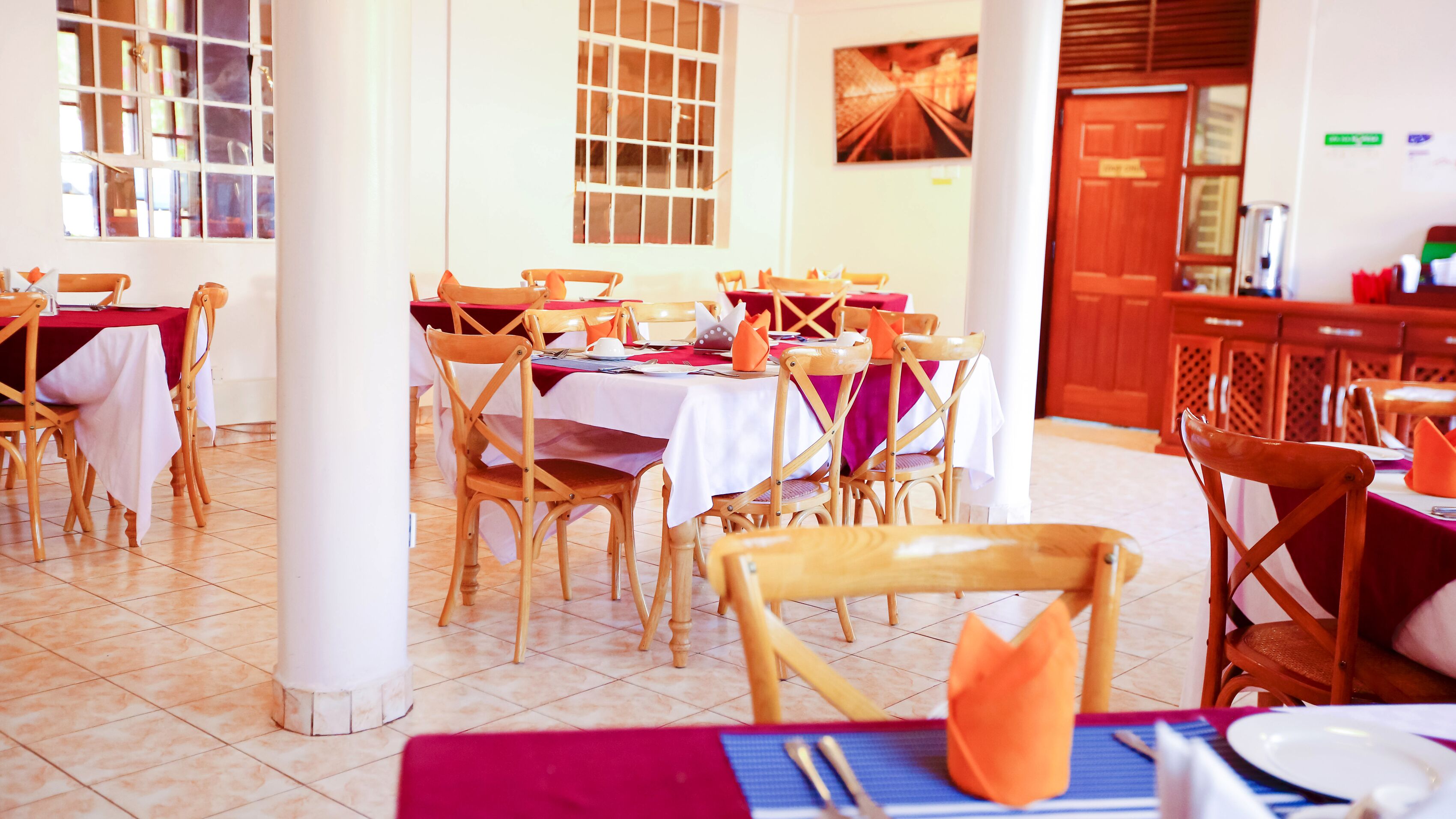 A restaurant with multiple tables and chairs, each set with white tablecloths and orange napkins.