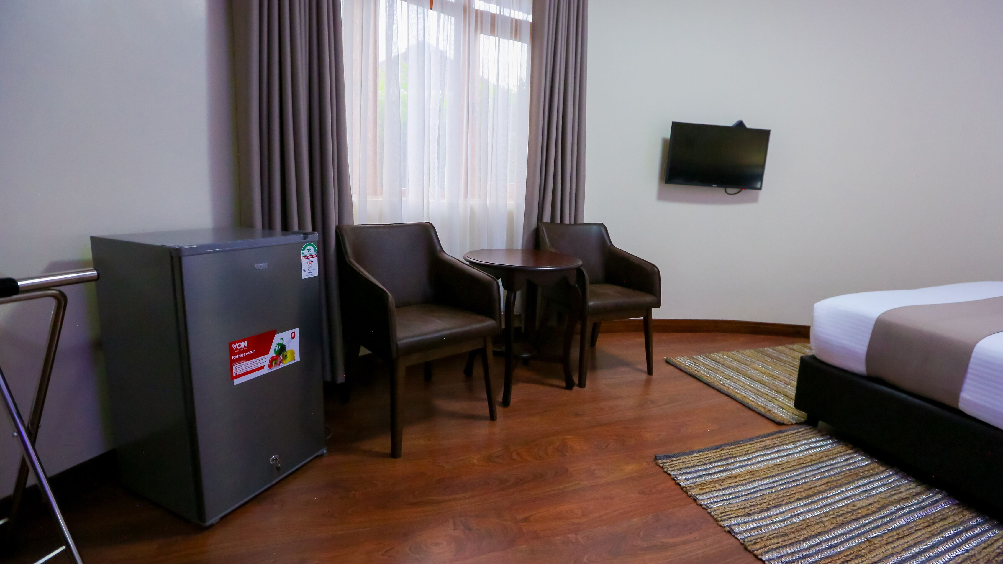Habitación de hotel con cama, una pequeña mesa con dos sillas, refrigerador y televisión en la pared.