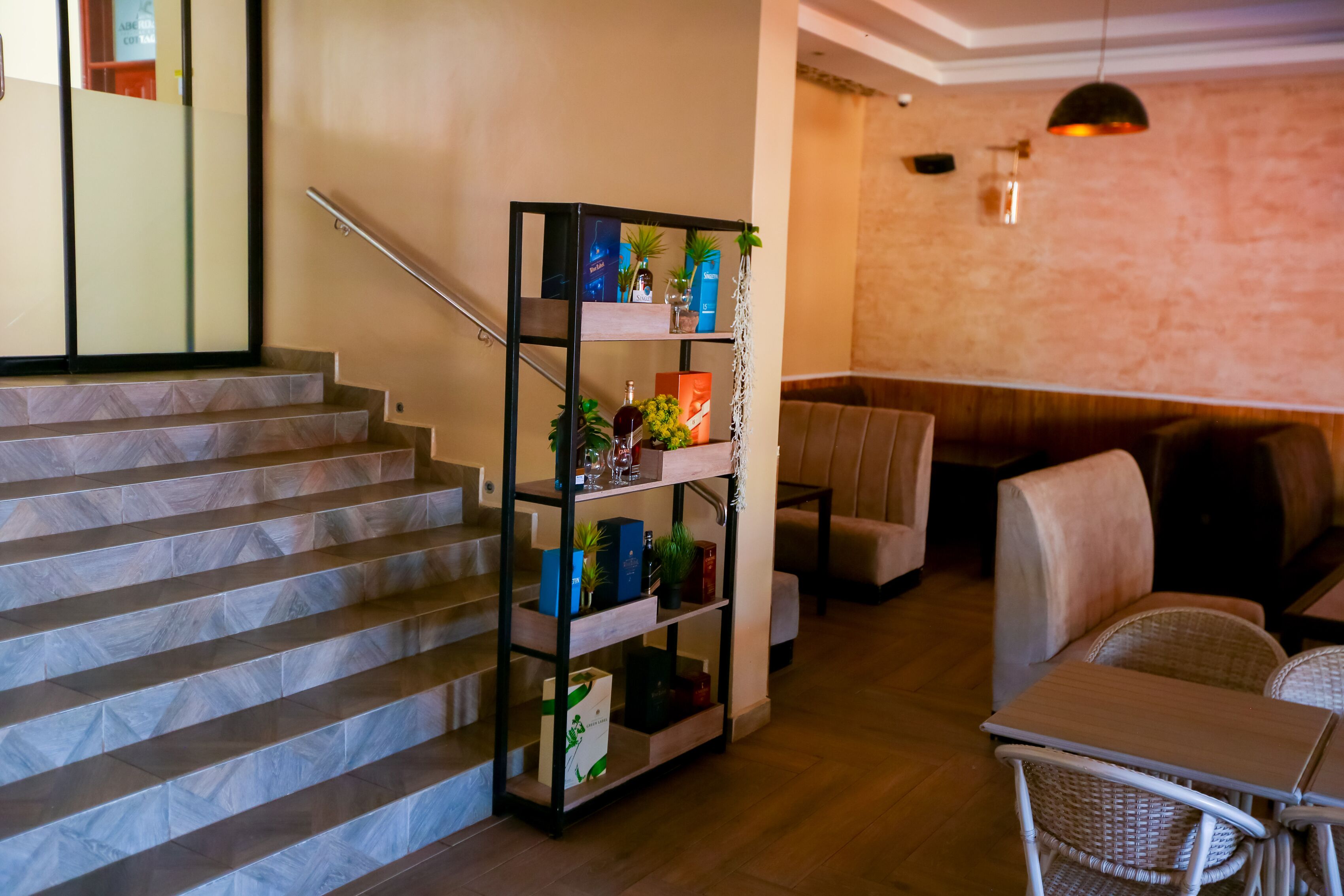 A staircase with a metal railing, a wooden floor, a seating area with wicker chairs, and a shelf with various items.