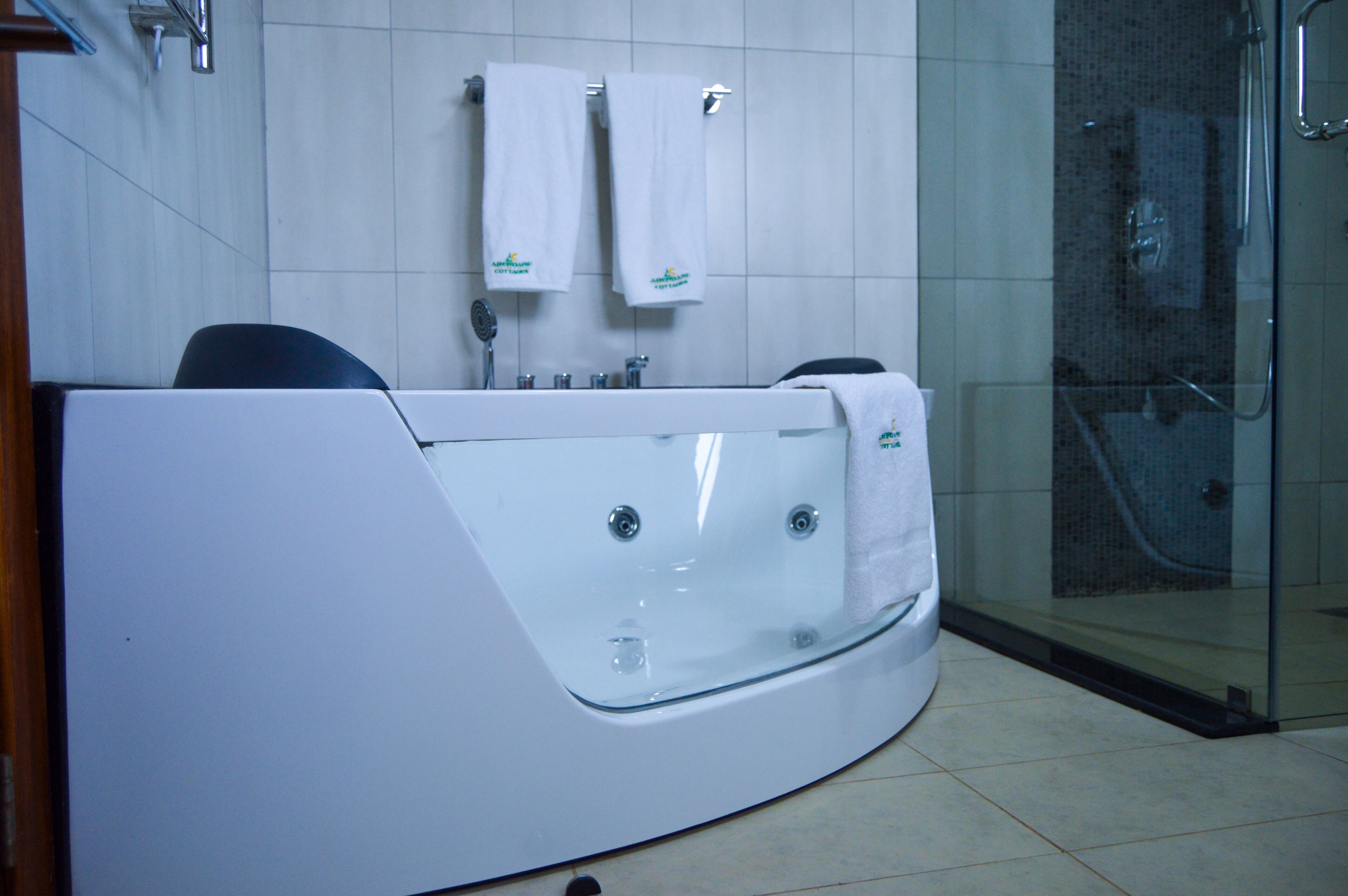 A modern bathroom with a large bathtub, a glass shower enclosure, and two towels hanging on the wall.