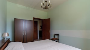 Ein Schlafzimmer mit einem Bett, einem Holzschrank, einem Sessel und einer Kandelaber.