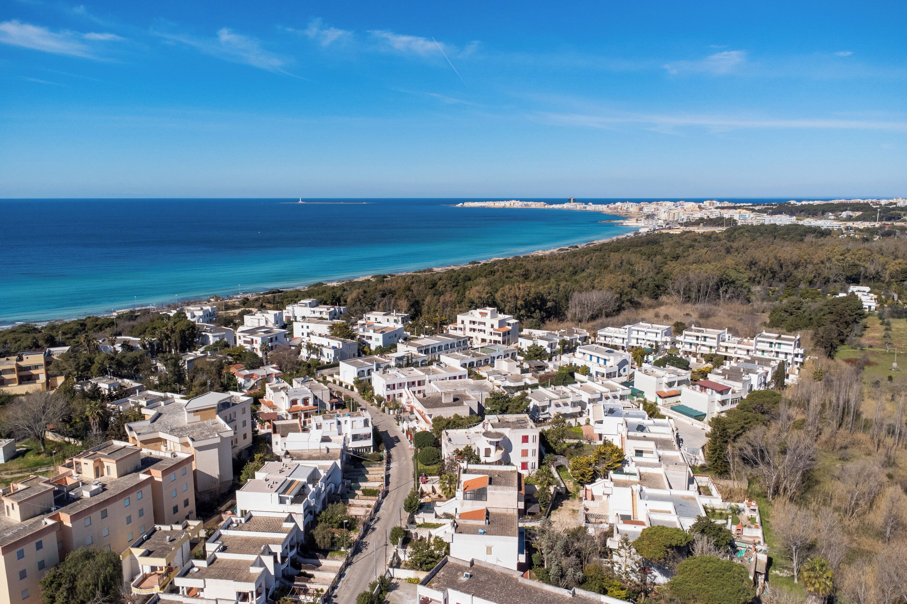 A coastal residential area with a mix of single and multi-story buildings, a clear view of the sea, and a distant lighthouse.