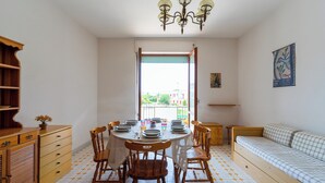 Ein Essbereich mit einem runden Tisch, gedeckt für vier Personen, Holzstühlen, einer Chandelieber und einem Sofa.