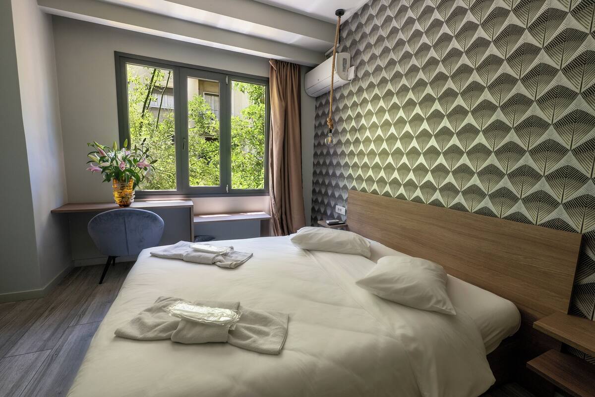 A hotel room with a bed, a desk, a chair, and a window with curtains.