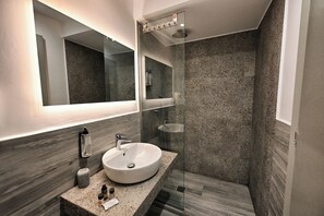 A modern bathroom with a granite countertop, a white sink, a glass shower enclosure, and a large mirror. - Urban Core Residence (Athens)