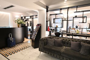 A modern hotel lobby with a black reception desk, a grey sofa, a patterned rug, and a decorative wall with shelves. - Urban Core Residence (Athens)