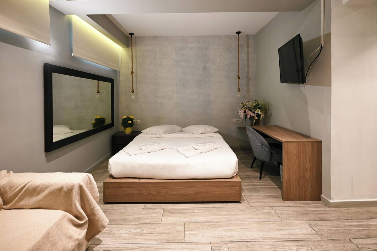 A modern bedroom with a large bed, bedside table, and a desk with a chair.