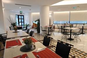 A modern dining area with multiple tables and chairs, some with plants. There are potted plants on the tables, and the floor has a geometric tile pattern. - Urban Core Residence (Athens)