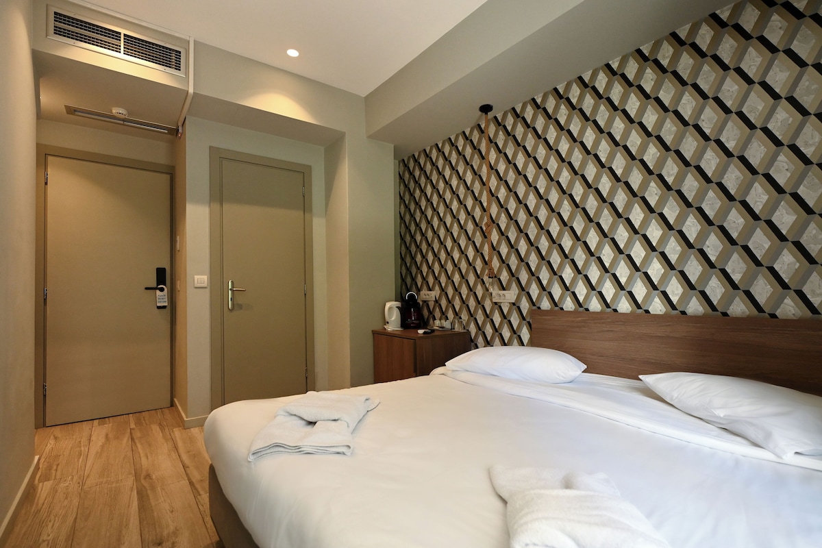 Ein Hotelzimmer mit einem ordentlich bezogenen Bett, einem hölzernen Kopfteil, einer Wand mit Muster, einem Nachttisch mit Lampe und einer Tür mit Griff.