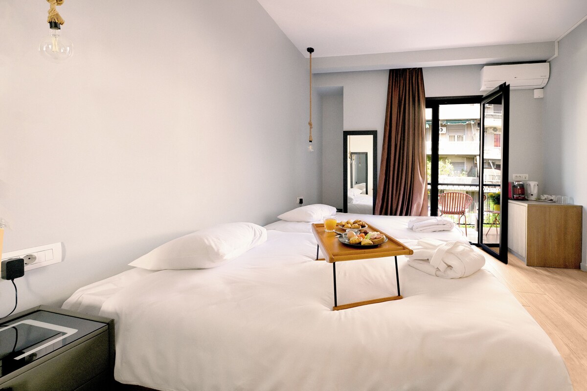 Camera d'albergo con un letto, un comodino con un vassoio per la colazione, una finestra con tende e un condizionatore d'aria.