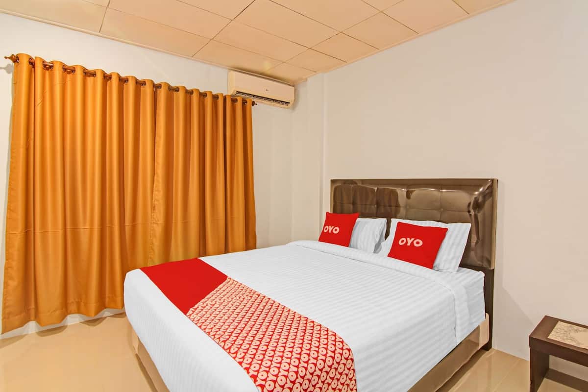 A hotel room with a bed, curtains, an air conditioning unit, and a bedside table.