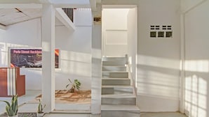 Un escalier menant à un niveau supérieur, un mur blanc avec une petite fenêtre et une affiche accrochée au mur.