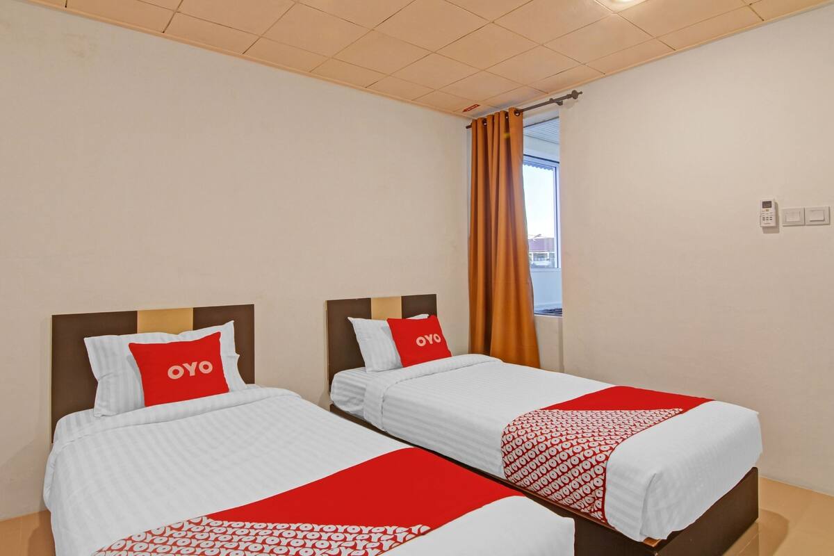 Two single beds with white bedding and red accents, a window with orange curtains, and a ceiling with a grid pattern.