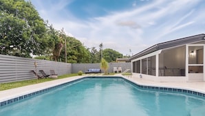 A swimming pool with a covered patio area, lounge chairs, and a wooden fence. - Charming and Amaizing Home with Pool in Miramar (Miramar)