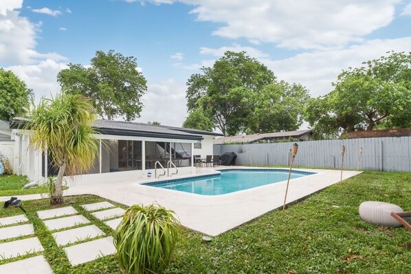 A backyard with a swimming pool, a covered patio, and a fenced area.