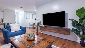 A modern living room with a blue sofa, a wooden coffee table, a TV mounted on the wall, and a large green plant. - Charming and Amaizing Home with Pool in Miramar (Miramar)
