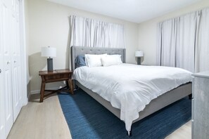 A neatly arranged bedroom with a bed, two bedside tables, a lamp, and a blue rug.
