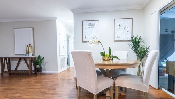A dining area with a round wooden table, four chairs, and a vase with flowers. There are two framed artworks on the wall, a small table with decorative items, and a potted plant. - Charming and Amaizing Home with Pool in Miramar (Miramar)
