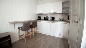 Una cocina compacta con armarios blancos, microondas, cafetera y dos taburetes de bar.
