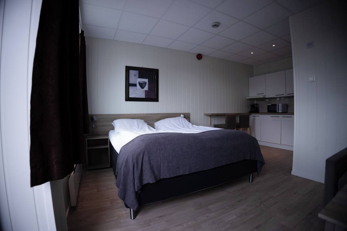 Ein modernes Schlafzimmer mit Bett, Nachttischen, einem kleinen Schreibtisch und einer Küchenzeile.