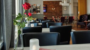 Interior de restaurante con una mesa lista para dos comensales, con un jarrón con una rosa roja, una vela y un posavasos.