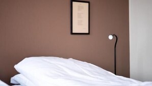 Una cama bien tendida con sábanas blancas en una habitación con pared marrón y un cuadro colgado encima.