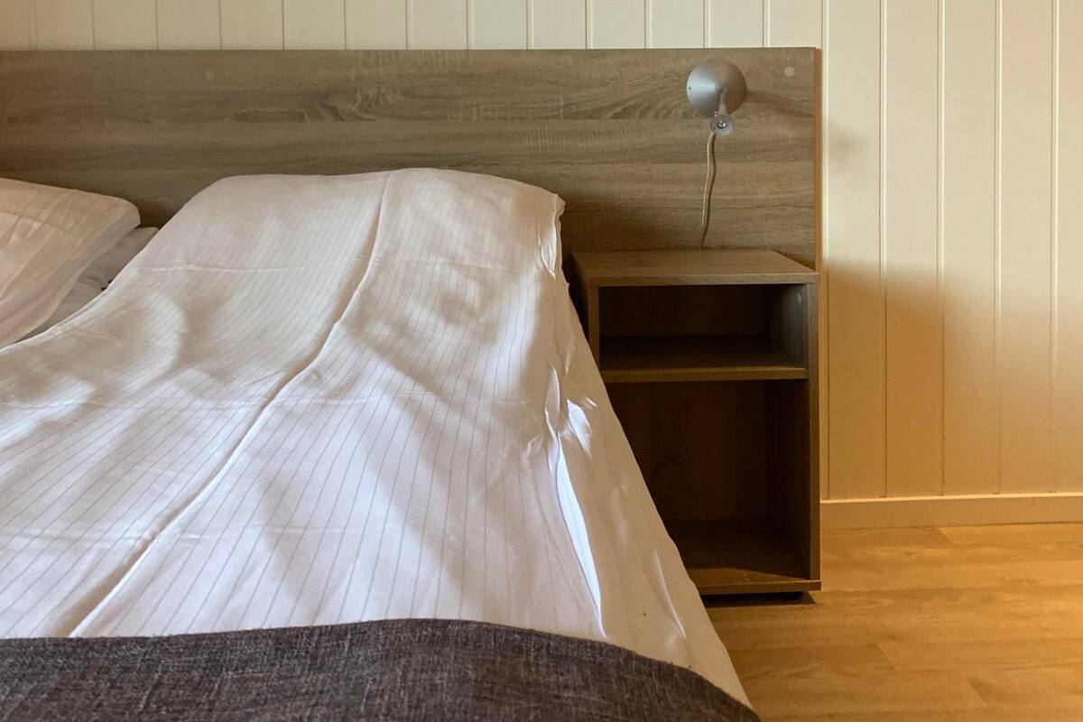 Ein Schlafzimmer mit hölzernem Kopfteil, einem Nachttisch und einem Rosenbild an der Wand.
