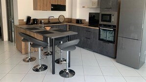 Eine moderne Küche mit einer zentralen Kochinsel, Barhocker, Backofen und einem Edelstahl-Kühlschrank.
