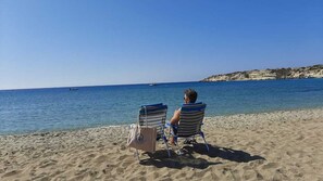 Two beach chairs with a bag on the sand near the water.