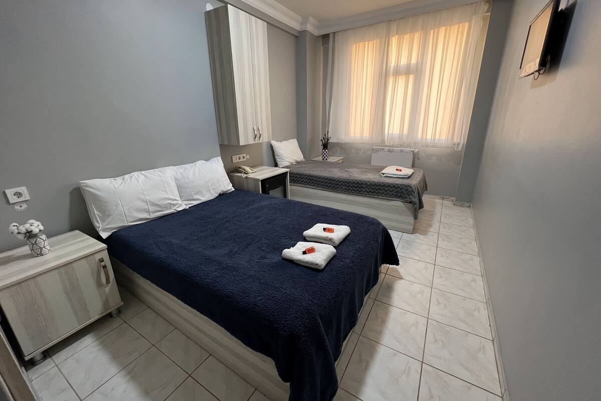 Un dormitorio con una cama grande, una cama más pequeña, una mesita de noche, un aparador y una ventana con cortinas.