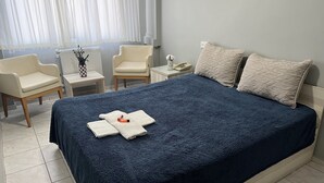A neatly arranged hotel room with a large bed, two chairs, a small table with a vase, and a nightstand with a phone. - Hotel Prima (Istanbul)