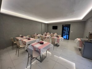 Un espace repas avec des tables dressées, un téléviseur à écran plat fixé au mur et une porte donnant sur l’extérieur.