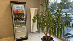 A vending machine stocked with beverages and a potted plant in a tiled area with a view of parked cars outside. - Hotel Prima (Istanbul)
