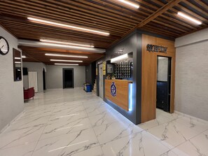 Een receptiegedeelte met een houten receptiebalie, marmeren vloer en een klok aan de muur.