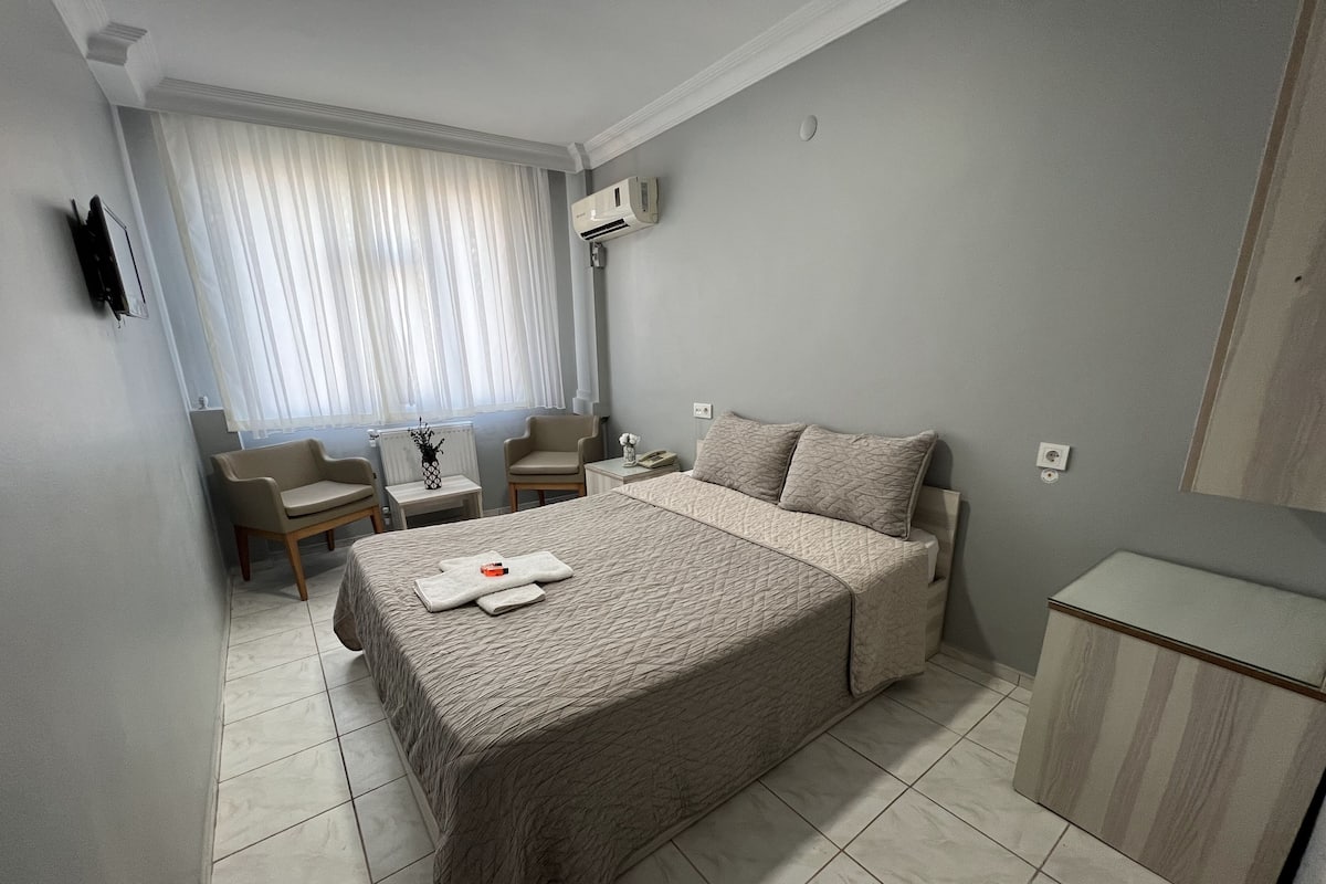 Una habitación de hotel con una cama, dos sillas, una mesita de noche y una ventana con cortinas.