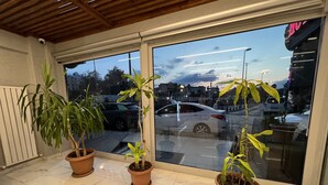 A hotel lobby with a tiled floor, three potted plants, a large window with a view of the street, and a ceiling with wooden beams. - Hotel Prima (Istanbul)