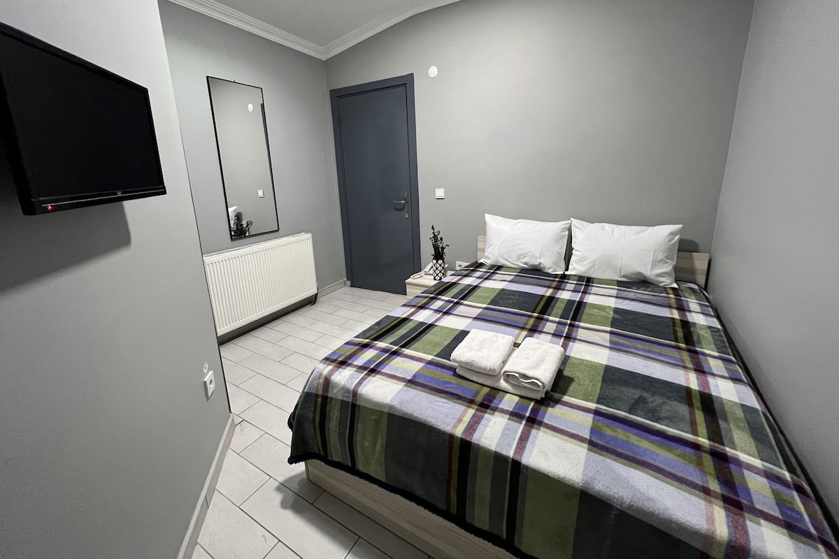 Un dormitorio con cama, televisor de pantalla plana montado en la pared, puerta y radiador.