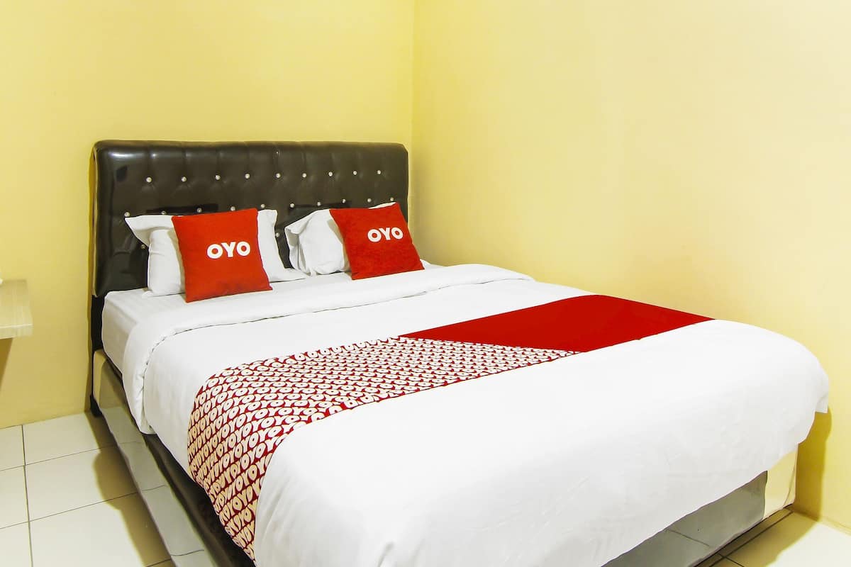 Uma cama com colcha estampada em vermelho e branco, duas almofadas vermelhas com a palavra 'OYO' e uma cabeceira escura.