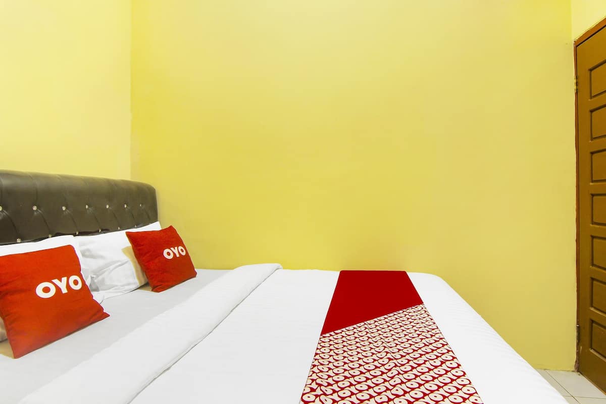 Uma cama com um cobre-leito branco e vermelho estampado, duas almofadas vermelhas com o texto "OYO" e uma cabeceira estofada cinza.