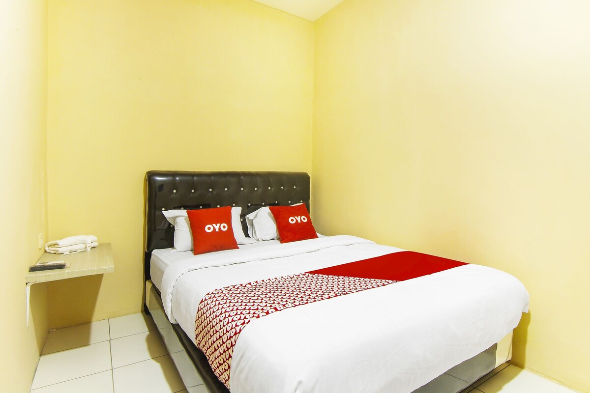 A hotel room with a bed, a nightstand, and a red and white bedspread.