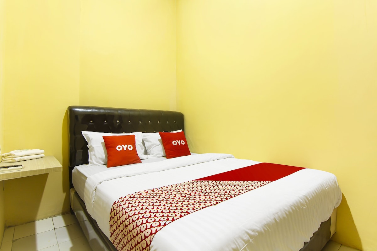 Quarto de hotel com cama, mesa de cabeceira e colcha estampada em vermelho e branco.