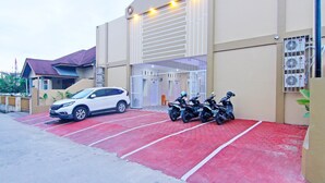 Un edificio con una zona de estacionamiento roja, un coche blanco y varias motocicletas aparcadas afuera.