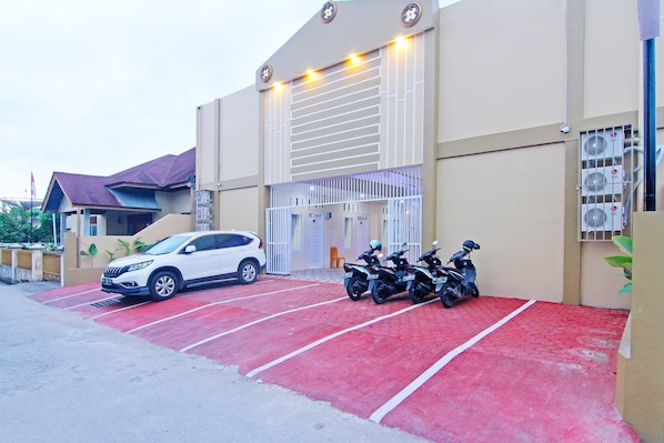 A building with a red parking area, a white car, and several motorcycles parked outside.