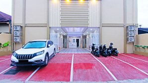 Un área de estacionamiento con una camioneta SUV blanca y varias motocicletas estacionadas frente a un edificio de fachada color beige y una entrada amplia.