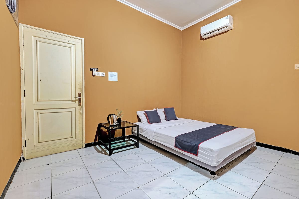 A room with a bed, a nightstand, a door, and an air conditioning unit.