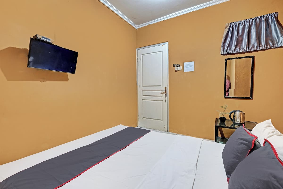 A hotel room with a bed, a television mounted on the wall, a door, a small table with a kettle, and a curtain.