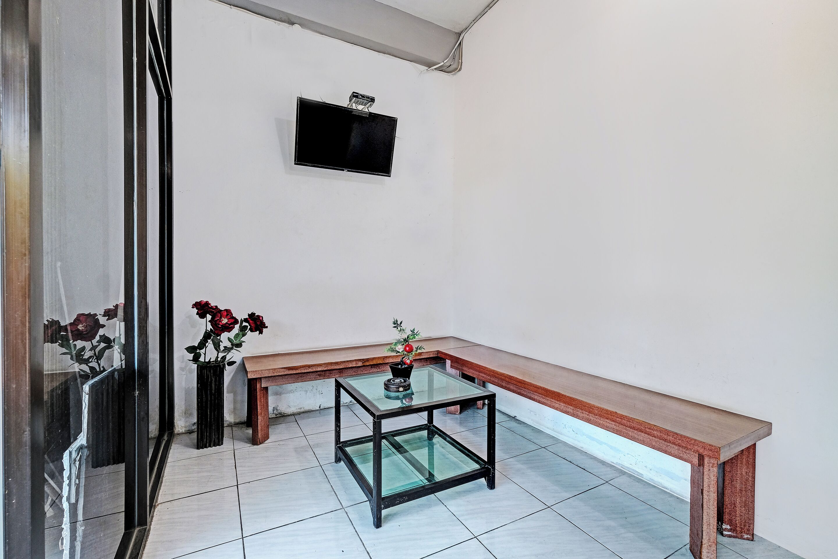 A room with a glass-top table, a wooden bench, and two potted plants.