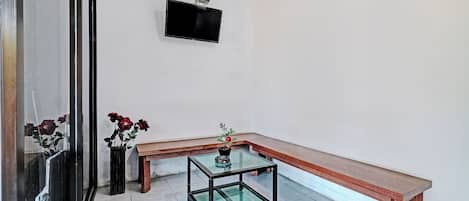 A room with a glass-top table, a wooden bench, and two potted plants.