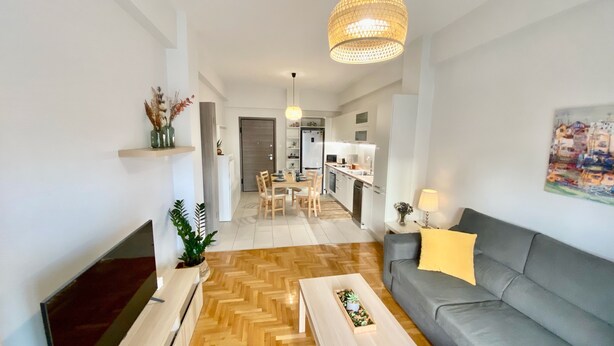 A modern living room with a grey sofa, a wooden coffee table, and a dining area with a wooden table and chairs. - GPK Lux 2BR | 7 min walking to Acropolis (Athina)