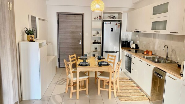 Une cuisine moderne avec des meubles blancs, un four encastré, un réfrigérateur et un coin repas comprenant une table et des chaises en bois.